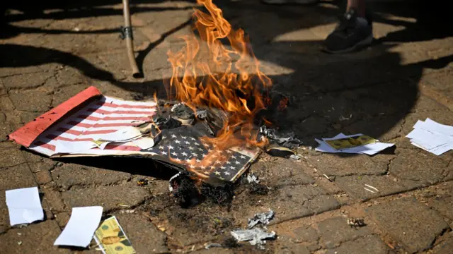 An American flag made out of cardboard is seen on fire on the ground