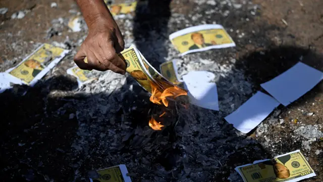 Mock US dollars with Trump's face on them lit on fire over a pile of ash