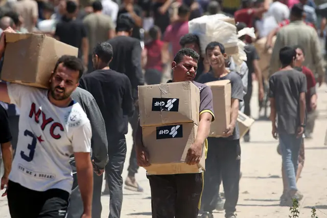 A man carries tow boxes of aid marked with the GHF logo