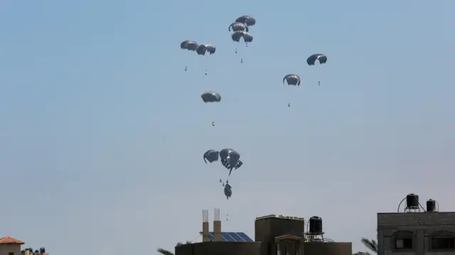 Aid packages, dropped from an airplane, descend over Gaza