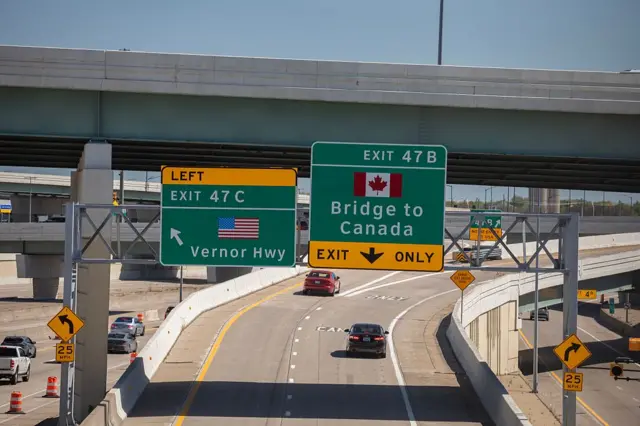 Road signs on a green and yellow backdrop indicating directions to enter the US and Canada near the US-Canada border