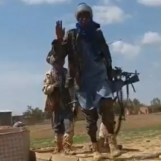 Fighters in Burkina Faso. They are walking along the periphery of an army base and carry heavy machine guns.