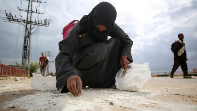 A woman collects spilled flour from the ground as Palestinians receive aid supplies