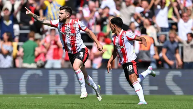 Ryan Manning celebrates scoring for Southampton, running with his arm outsretched, pointing his finger, with a teammate running next to him