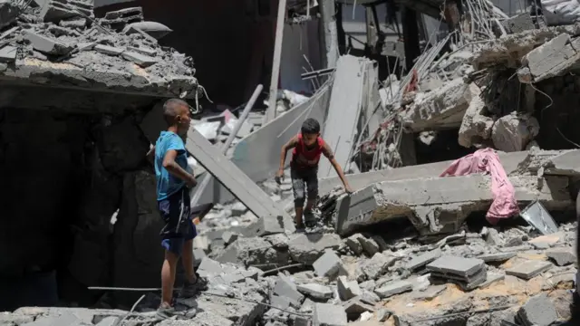 Palestinian boys inspect the site of an Israeli strike. The scene is of destroyed buildings.