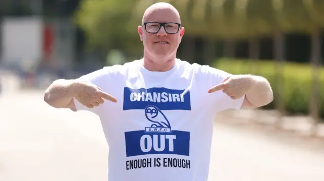 A Sheffield Wednesday fan wears a tshirt with the message "Chansiri Out: Enough is enough", while pointing to the message on his chest