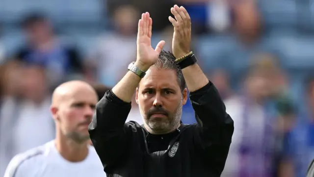 Marti Cifuentes applauds with his hands raised above his head
