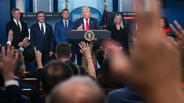 A raised hand in front of Donald Trump standing at a podium