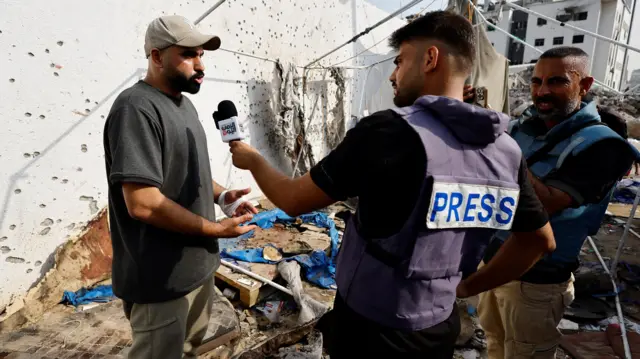 A journalist speaks to a man in a rubble-strewn street in Gaza