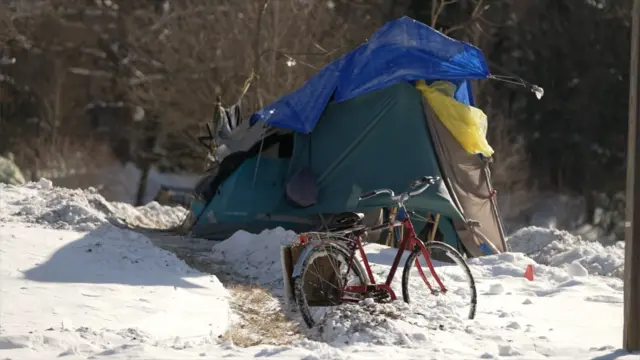 A snow-covered bike sits in front of a modified tent in the snow with trees behind