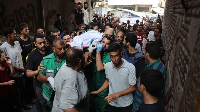 A crowd of people escort those carrying a white shroud through an alleyway