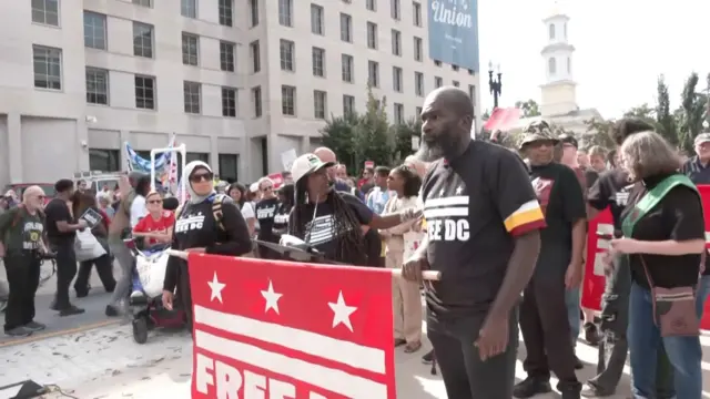 Protestors stand on the streets of Washington DC with signs and flags.