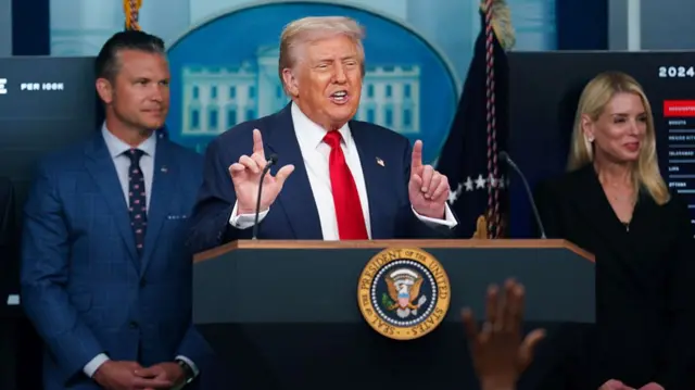 Donald Trump holds two hands in the air at a podium