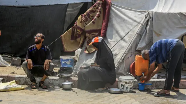 Three people sit on the street by a tent in Khan Younis