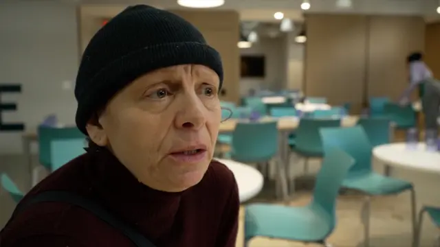 A woman wearing a black wool hat sits in an empty canteen