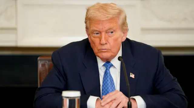 US President Donald Trump sits with his hands folding in the state dining room at the White House