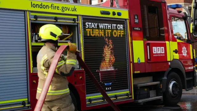 A firefighter carries a hose next to a fire engine