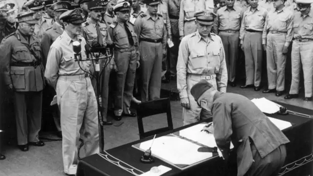 Japanese Imperial Headquarters representative General Yoshijiro Umezu (foreground, right) signing Japanese Instrument of Surrender while General MacArthur (foreground, centre) watches, aboard the USS Missouri, Tokyo Bay.