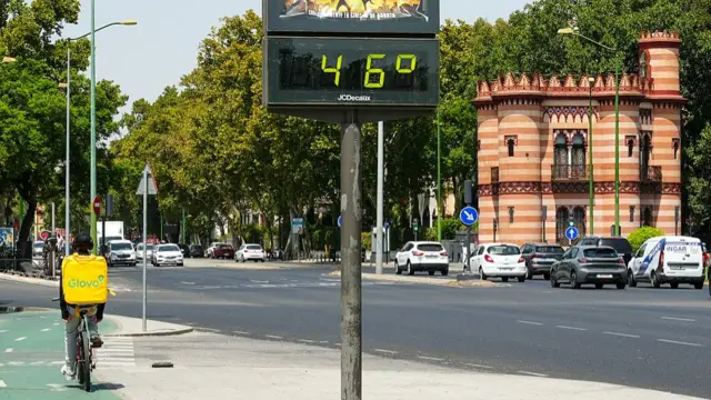 A cyclist in the streets of Seville, with a temperature sign showing 46 degrees on the pavement