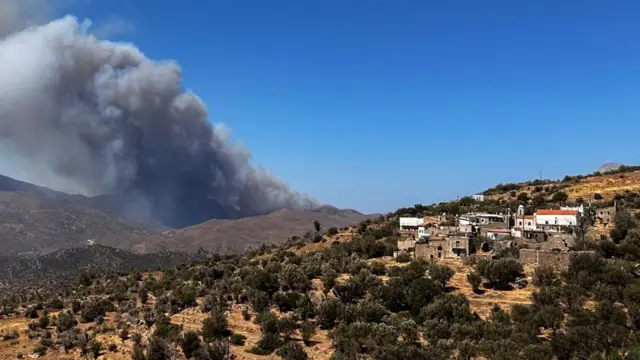 Plumes of smoke rises on the island of Chios, with some residential properties and large fields in the landscape.