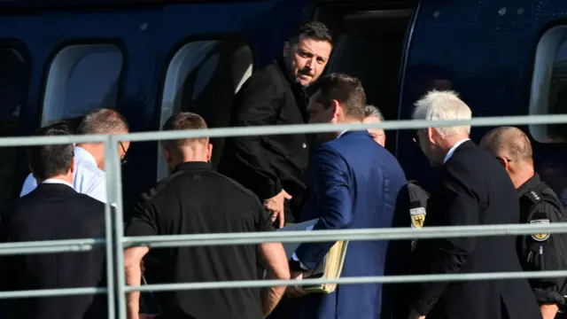 Volodymyr Zelensky boards a helicopter with group of people standing around him
