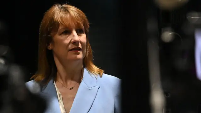 rachel reeves speaks to the media. she is wearing a powder blue suit. the photo is tightly cropped to her head and shoulders.
