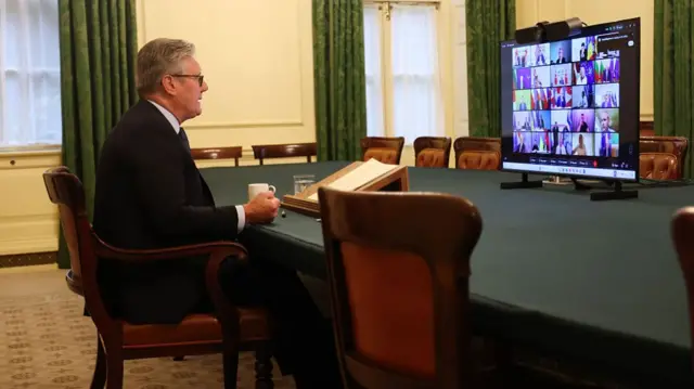 Keir Starmer sits in front of a TV that shows an ongoing video call.