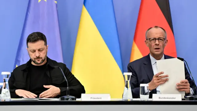 Zelensky and Merz sit at a table with flags behind them