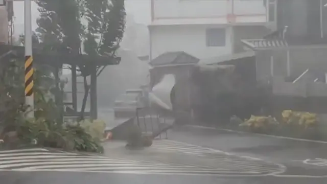 A screenshot from a video showing driving rain and heavy gusts blowing open a garage door