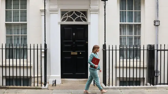 Chancellor Rachel Reeves wears a blue suit and walks passed No 11 Downing Street, holding a red folder.
