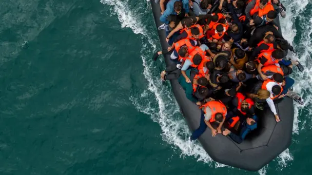 Drone shot of people in an inflatable boat crossing the English Channel The boat is extremely crowded and not everybody on board is wearing a life jacket.