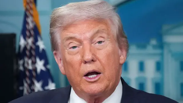 Headshot of Trump who speaks with mouth open as he looks at the camera with his eyes half shut