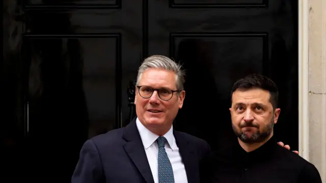 Zelensky and Starmer in front of a black front door, Starmer wears a blue suit and tie, Zelensky is in all black