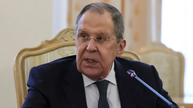 Russian Foreign Minister Sergei Lavrov, wearing a suit and tie, sits on a gold chair and speaks into a microphone. He's looking off to his right-hand side.