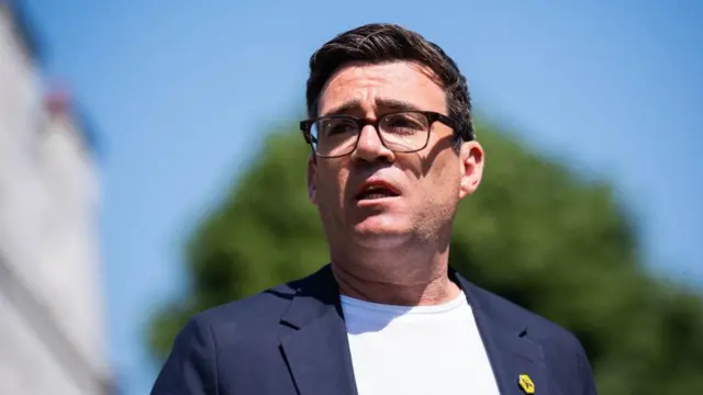 Headshot of Burnham who looks above and past the camera. He is outside in front of a tree and building which is blurry in the background