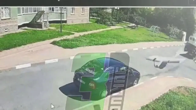 A screengrab of the video - filmed off a screen - where there is a grey drone to the right of a blue car