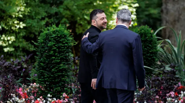 Starmer and Zelensky walk in the garden of Number 10. They walk away from the camera and Starmer has his arm on Zelensky's shoulder