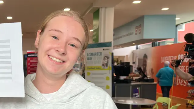 Olivia Melville smiles to camera and holds up her results