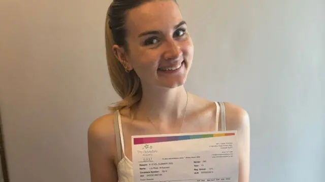 Lily-Rose holds up her A-level results. she is wearing leopard-print trousers and a white blouse.