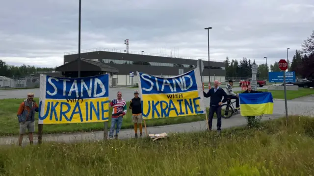 People hold 'Stand with Ukraine' signs on the Ukrainian flag.