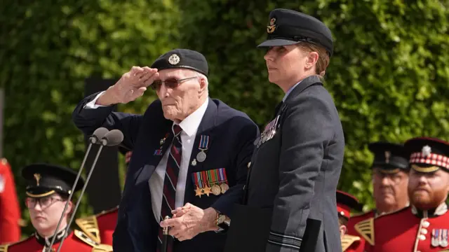 A veteran salutes next to a serving soldier