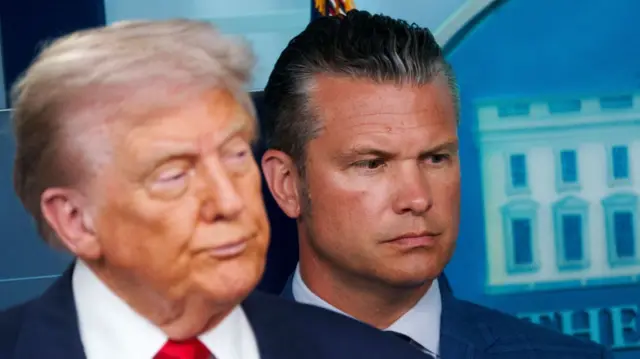 Donald Trump (L) blurred in the foreground with Defence Secretary Pete Hegseth in focus behind him. He's wearing a blue suit as he stands leaning on a blue background, the White House Logo affixed to the wall