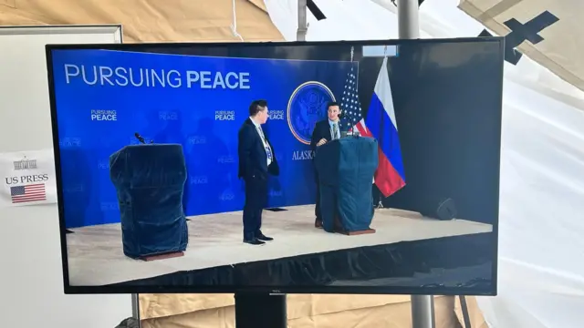 A TV screen showing podiums in front of a backing that says 'pursuing peace'