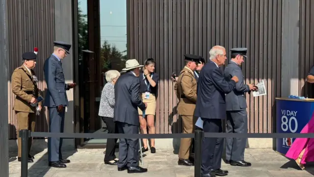 People in formal wear and some in military clothing queuing to go into the National Memorial Arboretum