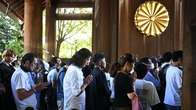 Crowds of people walking in the shrine with their heads lowered and hands pressed together in prayer
