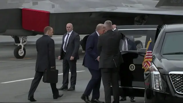 Donald Trump in a black suit enters the presidential limousine, nicknamed The Beast, on the tarmac in Elmendorf-Richardson base in Anchorage
