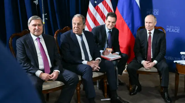 The men sit in a row in front of US and Russian flags