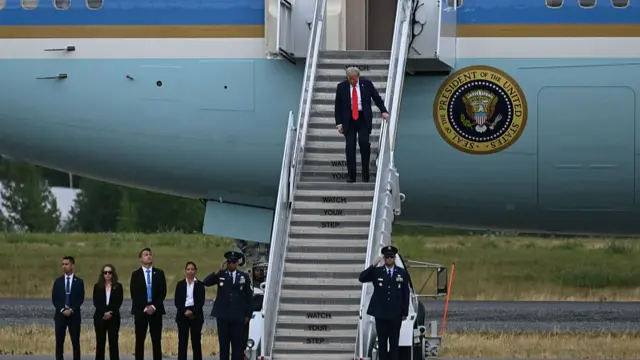 Donald Trump in black suit walks down steps of Air Force One after landing in Alaska