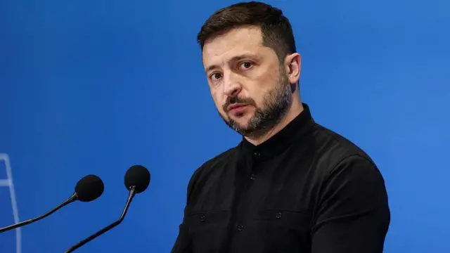 Zelensky at a podium in a black shirt before a blue background