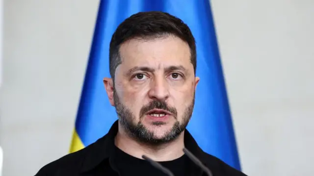 A file photo of Zelensky speaking - he is standing in front of a microphone with a Ukrainian flag behind him